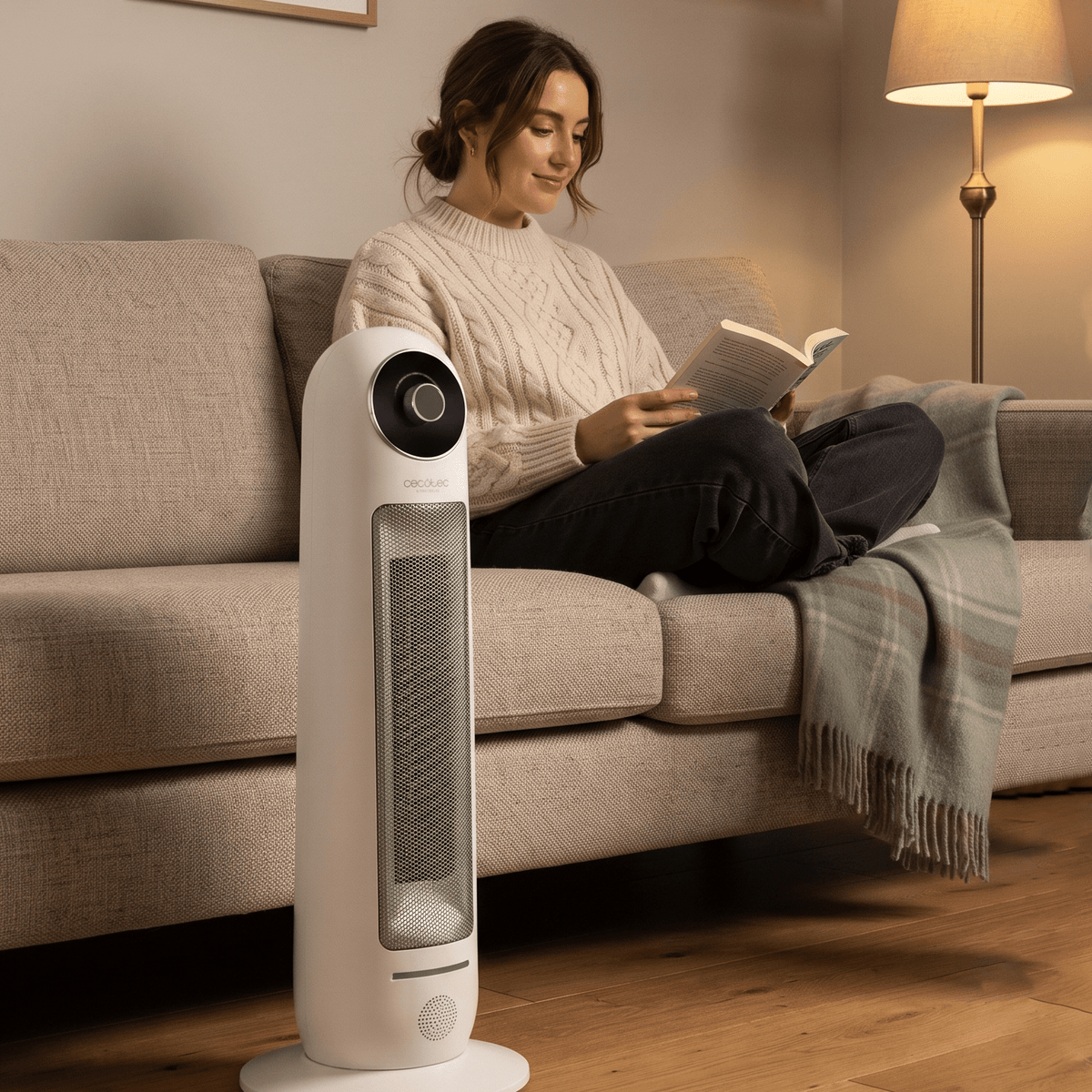 Woman reading on sofa next to quiet white ceramic tower heater in warm living room.