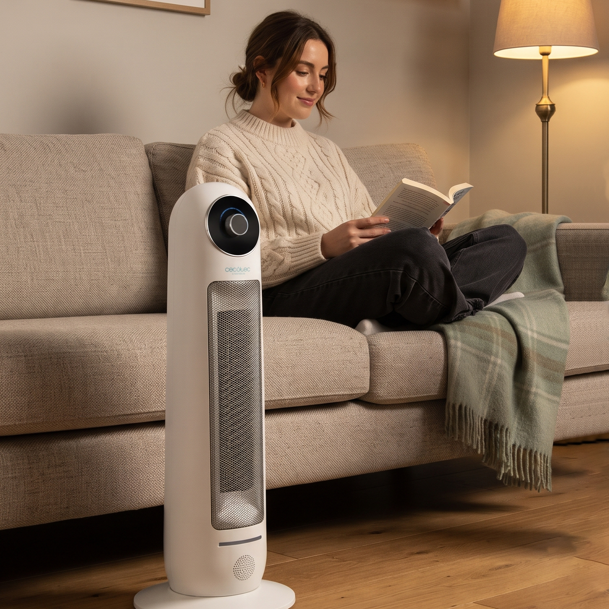 Woman reading on sofa next to quiet white ceramic tower heater in warm living room. 