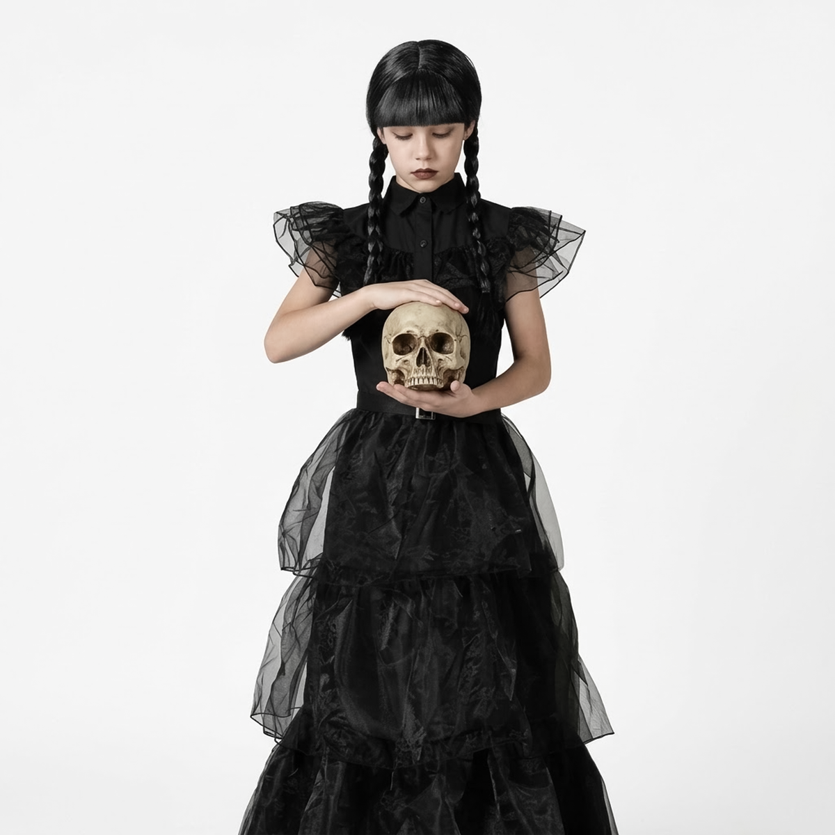 Studio portrait of girl wearing black tiered girls gothic prom dress holding skull prop. 