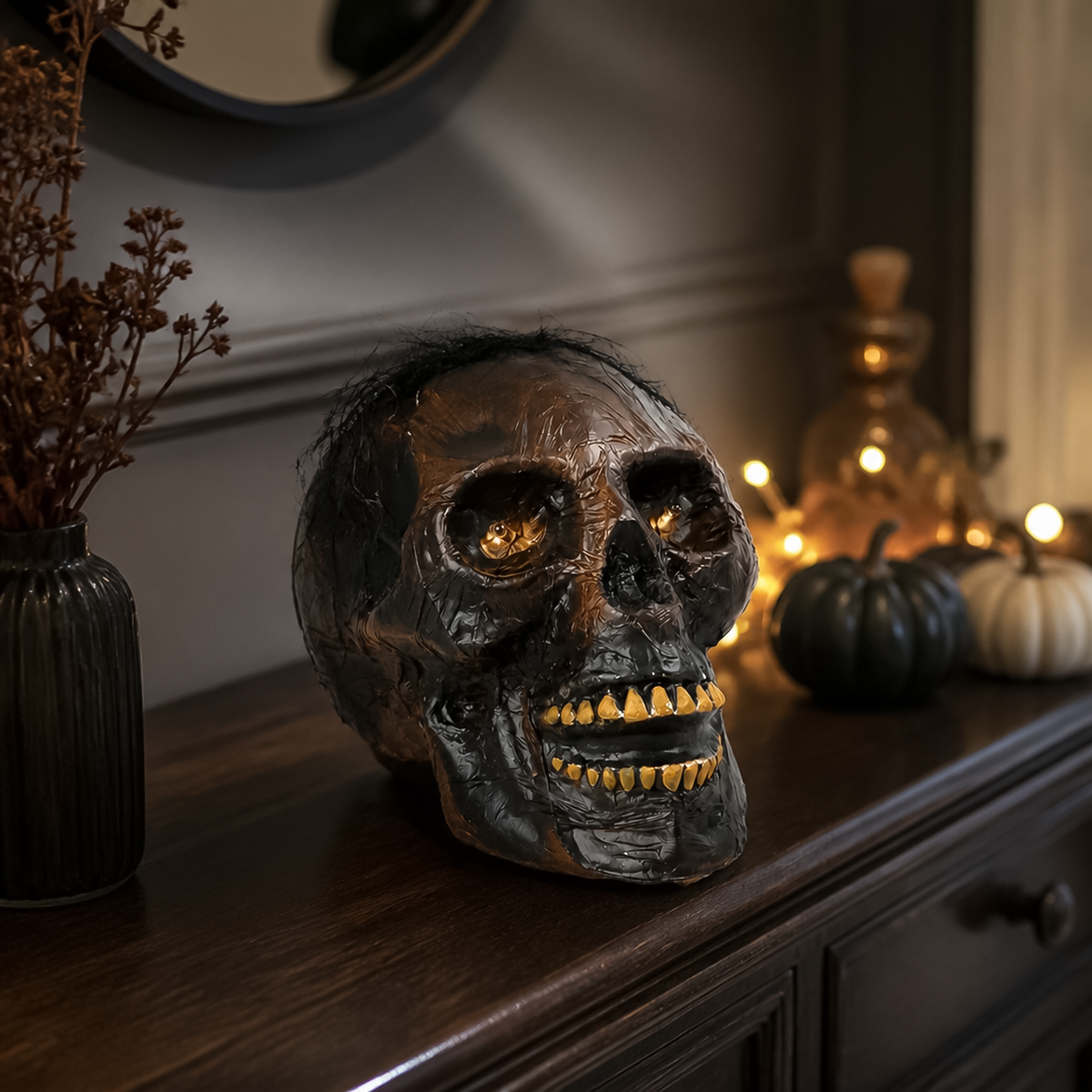 Light up skull halloween decoration positioned on dark wood sideboard next to pumpkins and fairy lights.